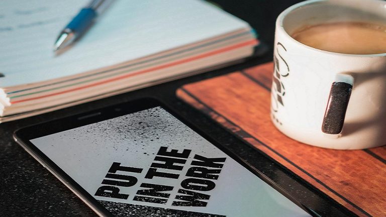 workspace with coffee, paper pad and tablet with the words 'Put in the work' displayed