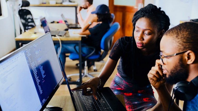 a man and a woman sitting at a computer desk talking